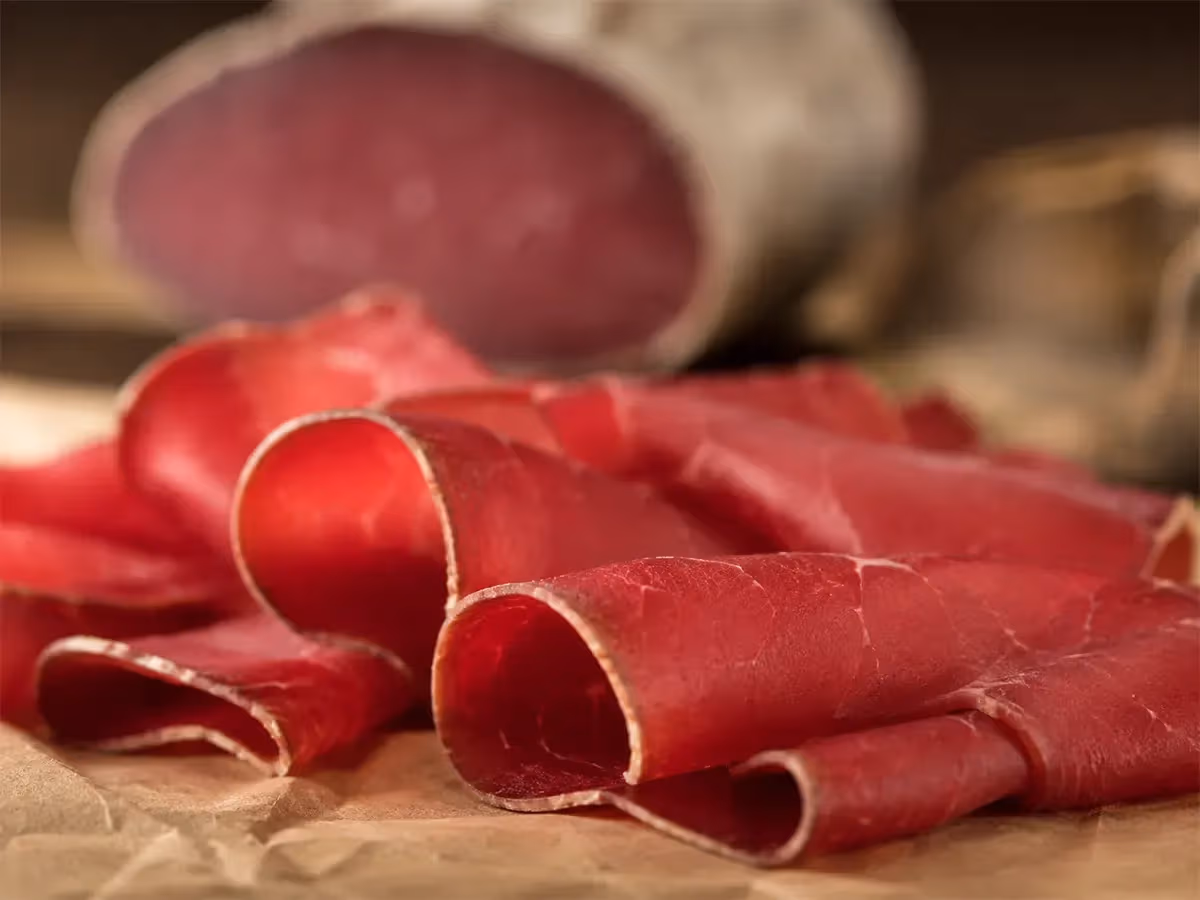 Fette sottili di bresaola rosse arrotolate su carta da macellaio con pezzo intero sfocato sullo sfondo