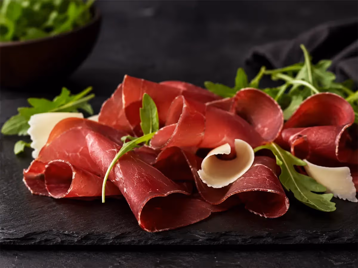 Bresaola affettata con rucola fresca e scaglie di formaggio su ardesia nera sfondo scuro