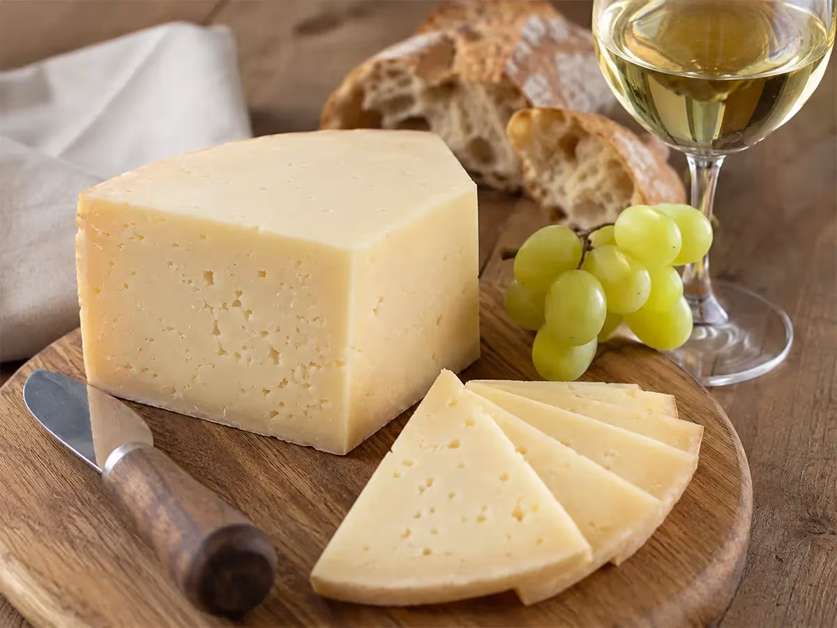 Asiago DOP a fette su tagliere in legno con uva bianca pane rustico e calice di vino bianco