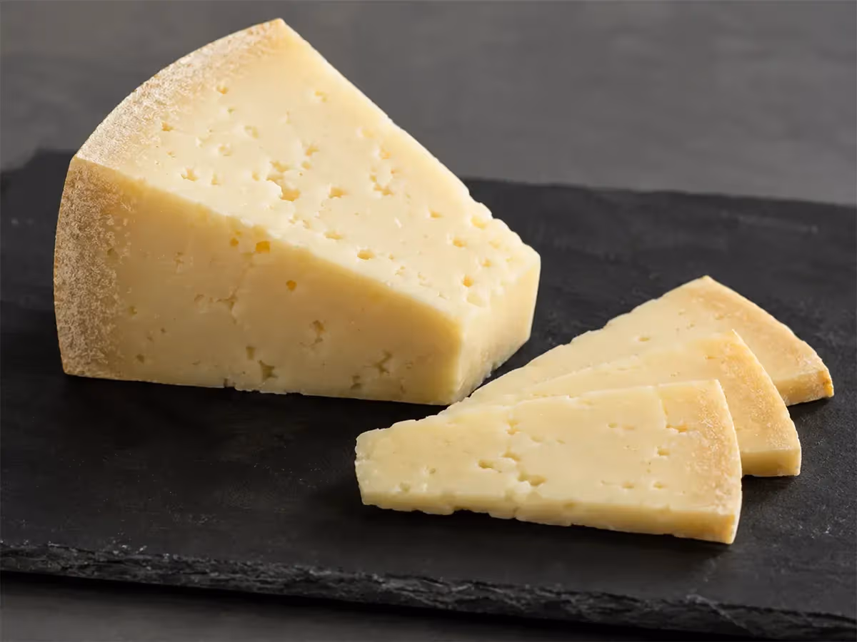 Spicchio di Asiago DOP con crosta naturale e fette sottili disposte a ventaglio su ardesia grigia
