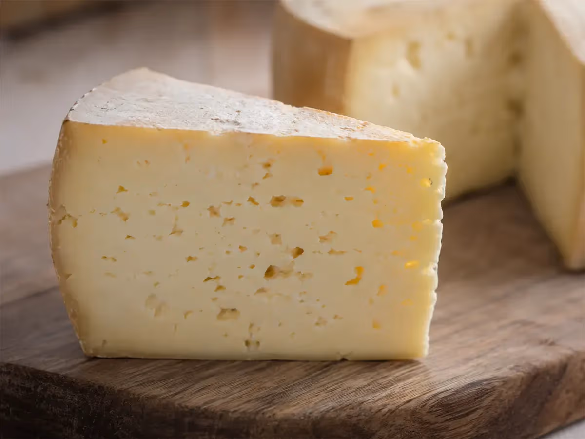 Primo piano di un cuneo di formaggio stagionato pasta paglierina con occhiatura irregolare su legno