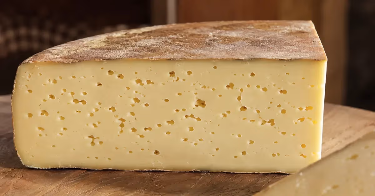 Fetta di Fontina d'Aosta DOP con pasta giallo paglierino e piccoli occhi su tagliere in legno