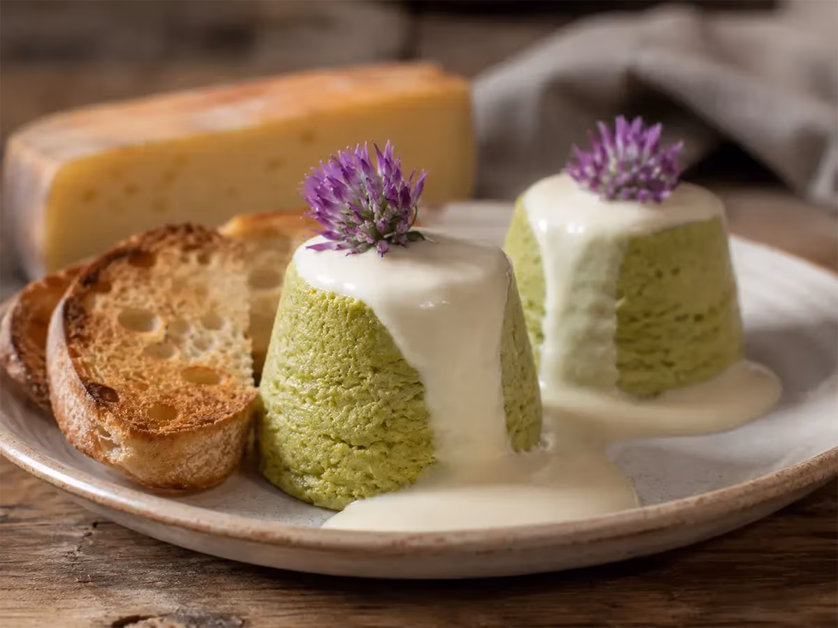 Due sformatini verdi con fonduta di Fontina e fiori viola di erba cipollina su piatto rustico