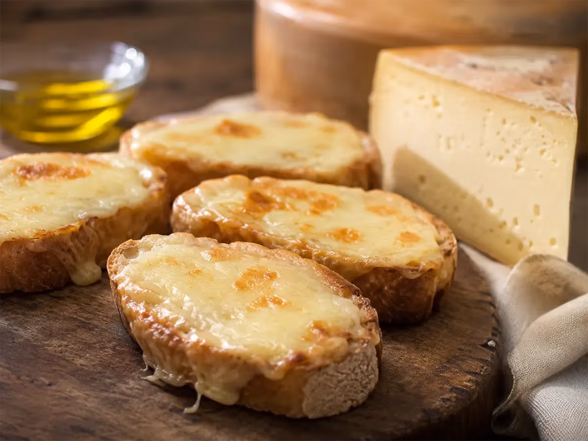 Crostoni di pane tostato gratinati con Fontina filante dorata su tagliere di legno