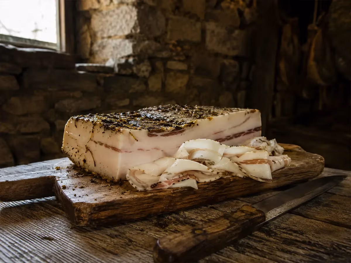 Blocco intero di lardo di Arnad DOP con crosta di erbe aromatiche e coltello su tavolo rustico in pietra