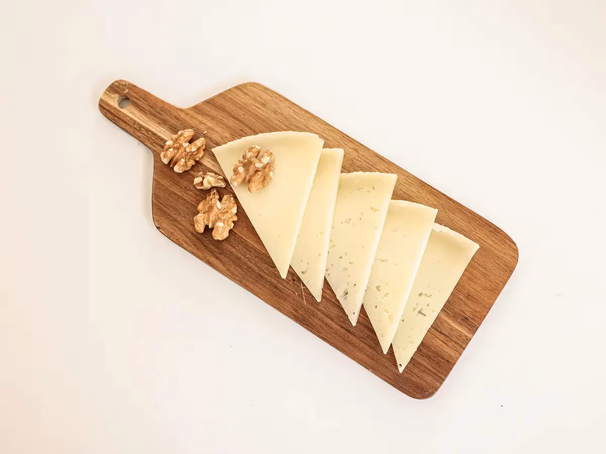 Fette triangolari di Montasio DOP a pasta chiara disposte a ventaglio con noci su tagliere