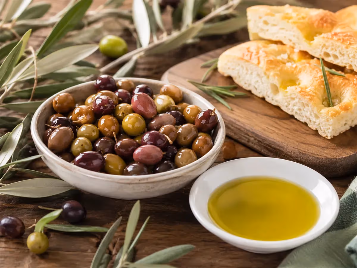 Ciotola rustica di olive miste colorate accanto a focaccia dorata e scodellino di olio giallo