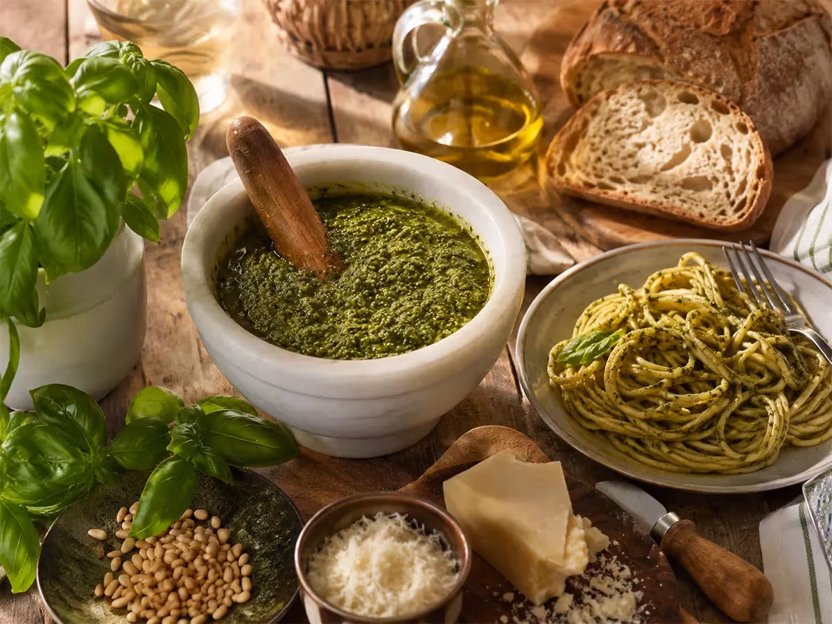 Mortaio di marmo con pesto genovese accompagnato da spaghetti al pesto pane rustico e parmigiano