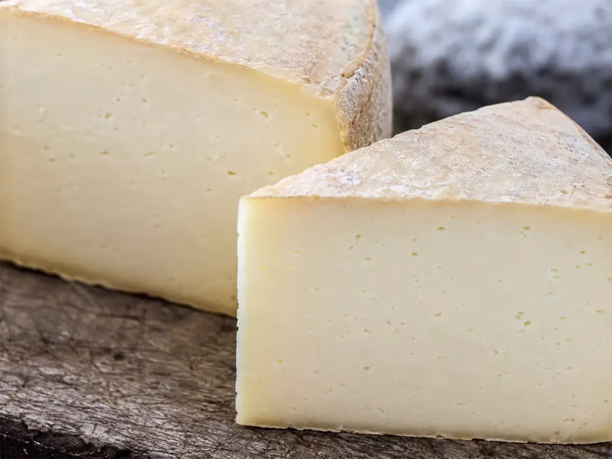 Primo piano di due spicchi di Toma a pasta bianco-avorio con crosta naturale su legno scuro