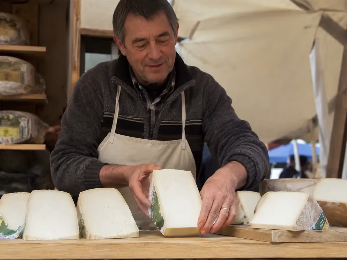 Venditore di mercato sistema porzioni di Toma Ossolana bianca su bancone all'aperto