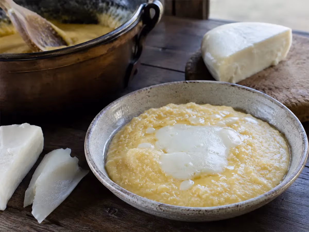 Polenta cremosa gialla con formaggio fuso al centro e pezzi di Toma bianca accanto in ciotola rustica