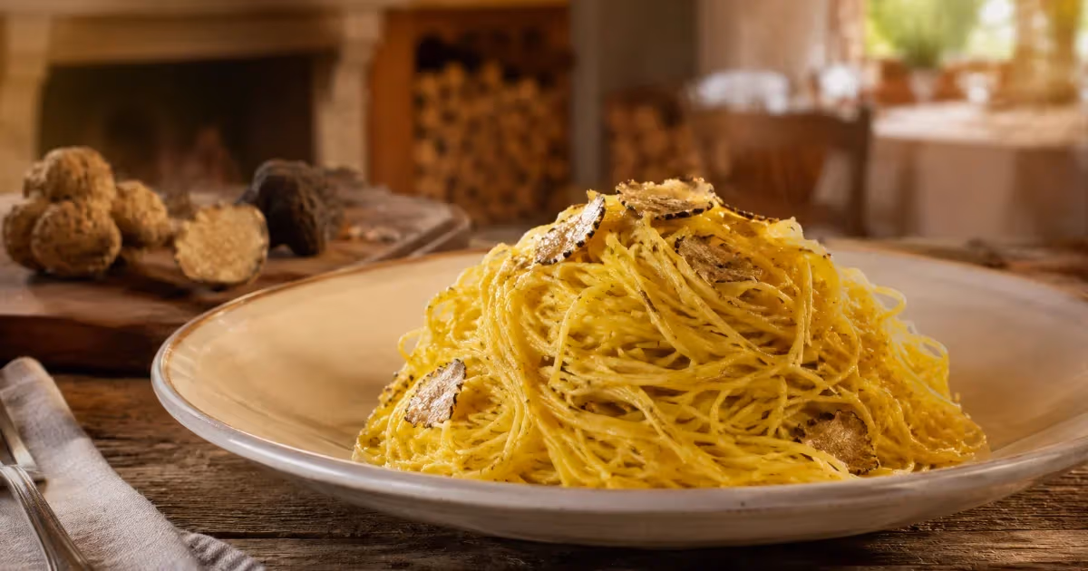 Tajarin piemontesi al tartufo nero in piatto rustico bianco con scaglie scure su tavolo in legno
